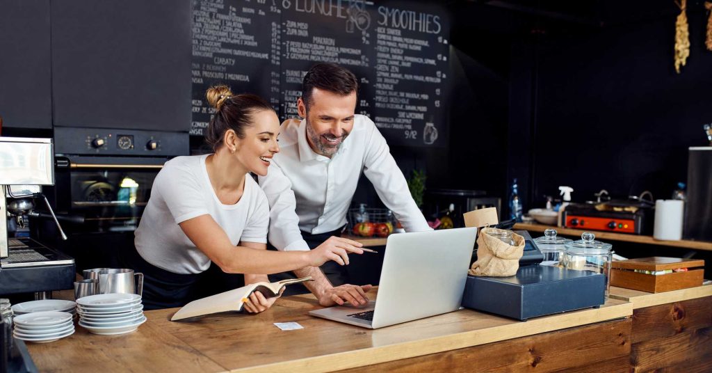 Two cafe owners working together planning supply orders on laptop