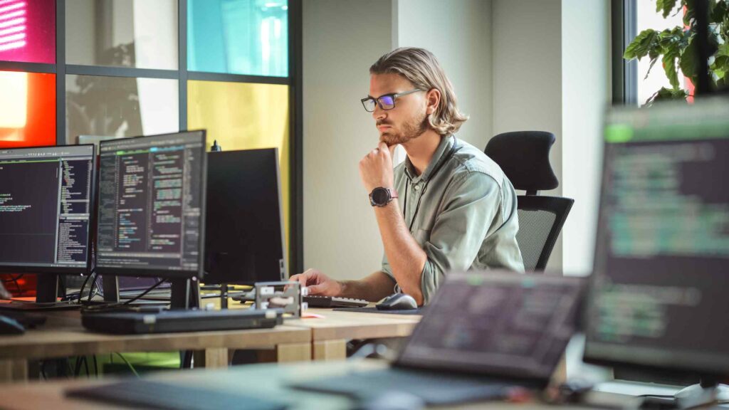 Focused Caucasian Man Coding On Desktop Computer in Stylish Office Space. Male Software Engineer Developing Innovative Application For Business Customers in Technological Start-up Company.